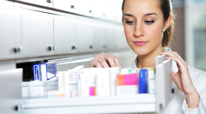 Young female pharmacist reaching for medicine